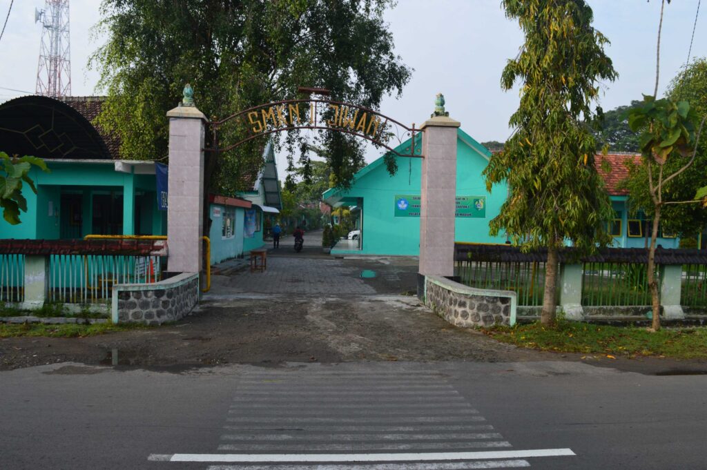 Foto tampak depan SMK Negeri 1 Jiwan Madiun, sekolah jurusan TKJ dengan laboratorium jaringan lengkap.